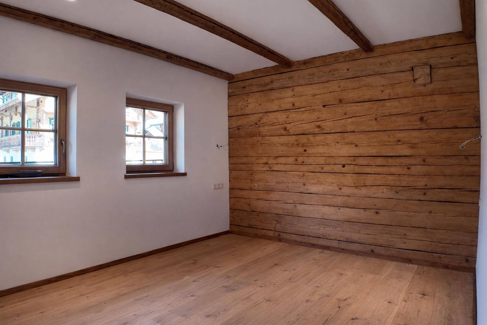 Helles Schlafzimmer mit Holzwand, weißen Wänden und sichtbaren Deckenbalken.