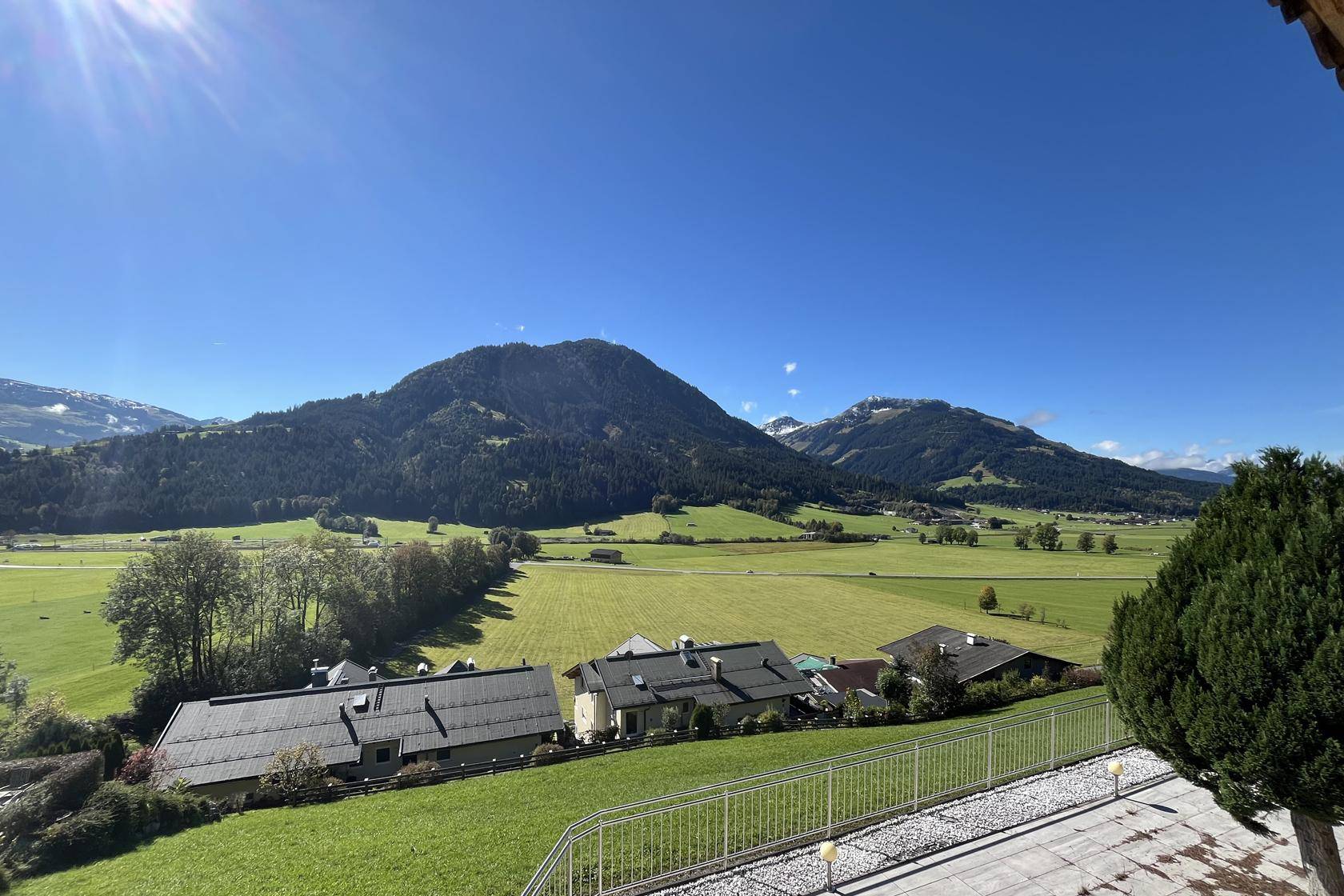 Atemberaubender Fernblick über das Tal mit grünen Wiesen, bewaldeten Hängen und schneebedeckten Gipfeln.