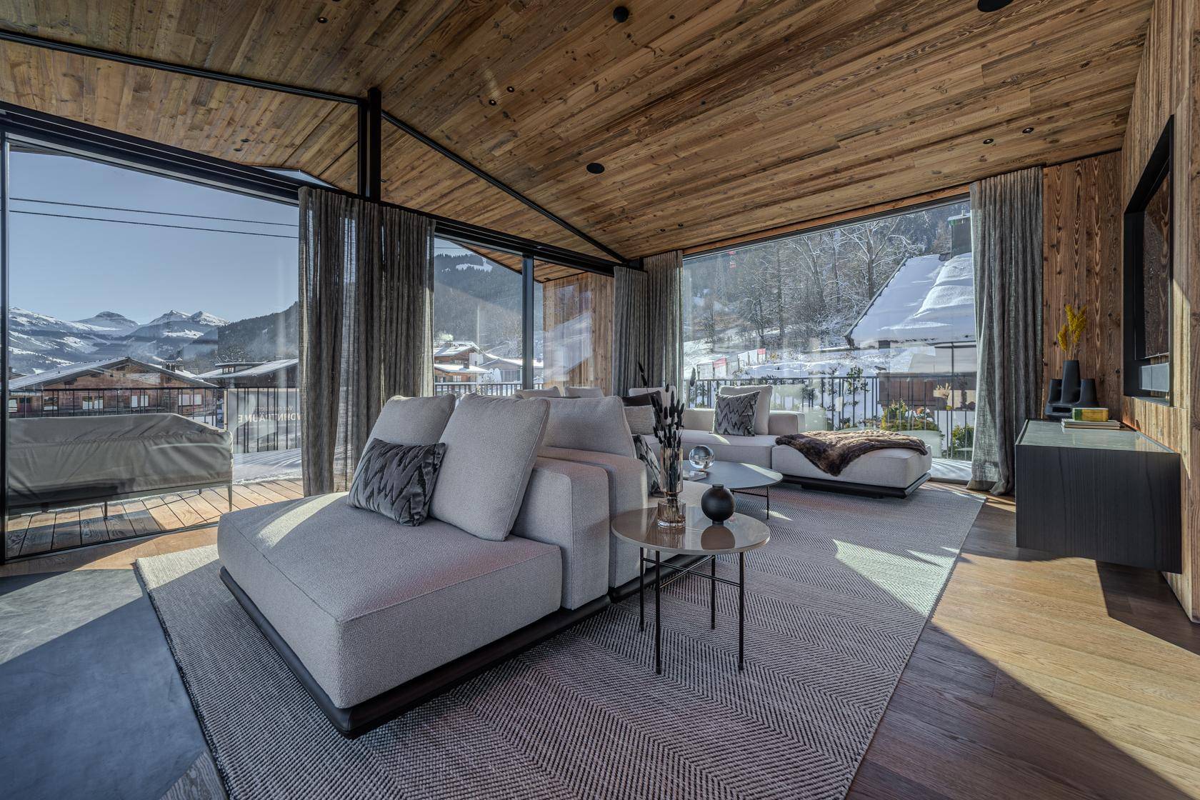 Elegantes Wohnzimmer mit bequemen Sofas, Teppich und großen Fenstern mit Blick auf die verschneite Landschaft.