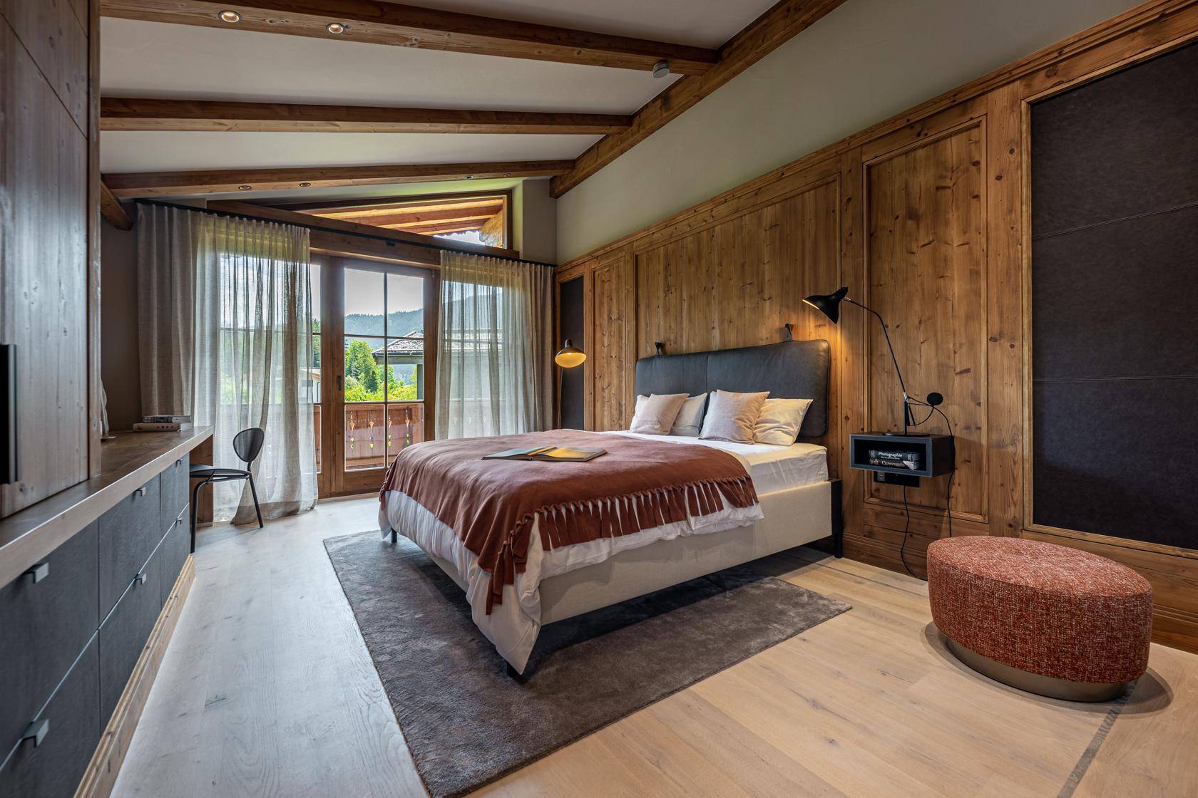 Gemütliches Schlafzimmer mit Holzwänden, hoher Decke und Zugang zu einem Balkon mit Bergblick.