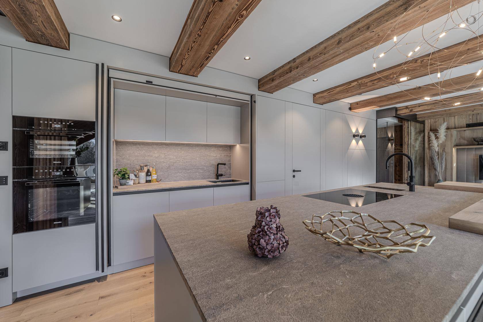 Hochwertige moderne Küche mit Stein-Arbeitsplatte, integrierten Geräten und Holzbalken.