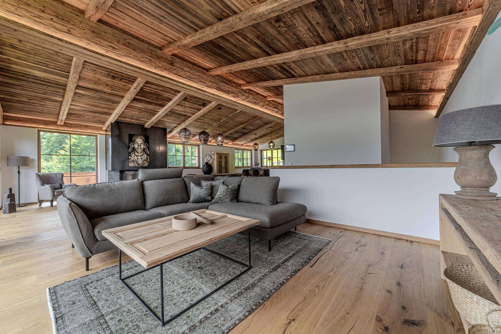 Gemütlicher Wohnbereich mit Ecksofa, Holzbalkendecke und Blick auf die umliegende Natur.