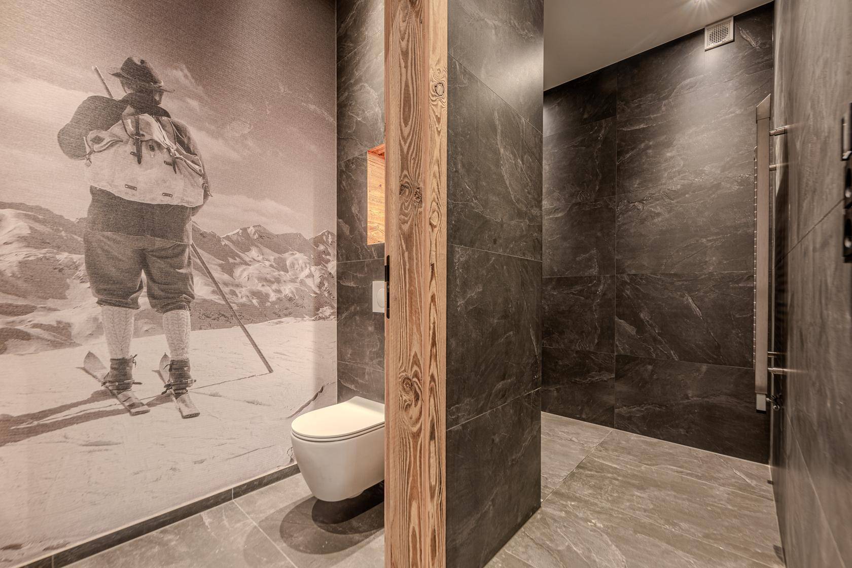 Modernes WC mit dunklen Fliesen, Wand-WC und alpiner Wanddekoration.
