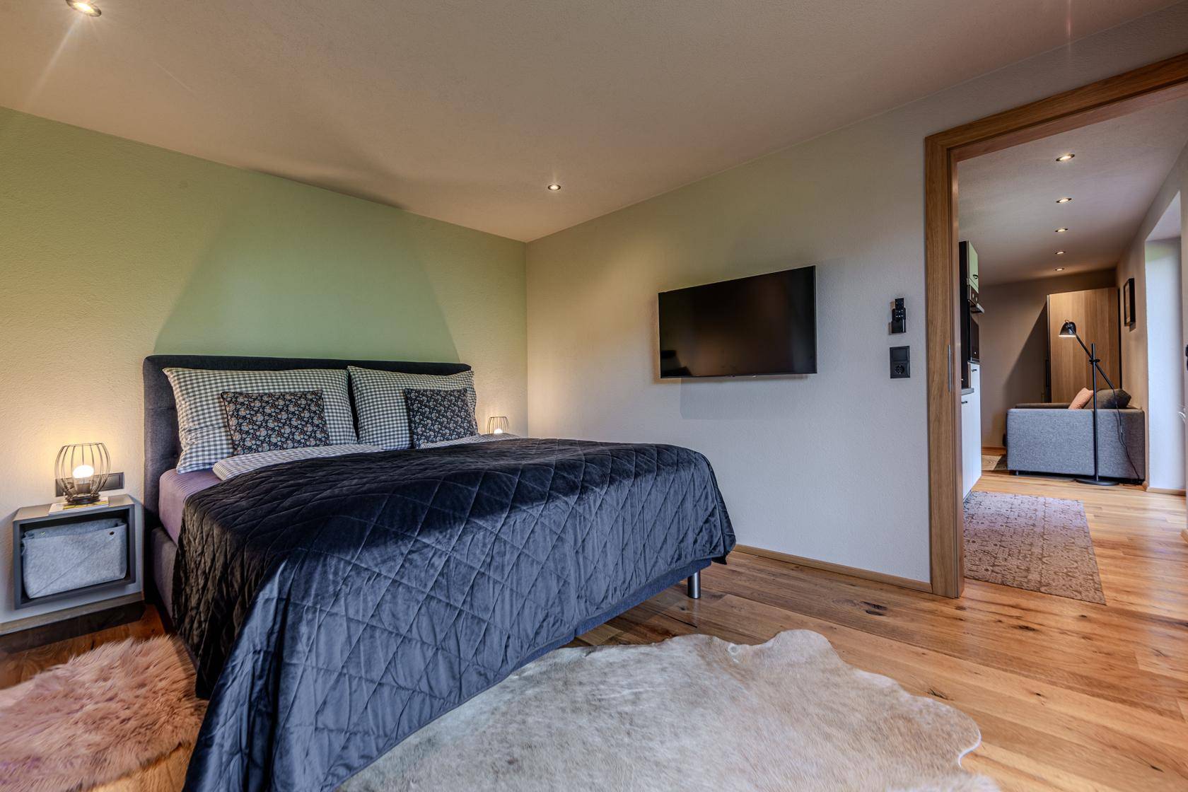 Komfortables Schlafzimmer mit Holzboden, Wandfernseher und Zugang zum Flur.