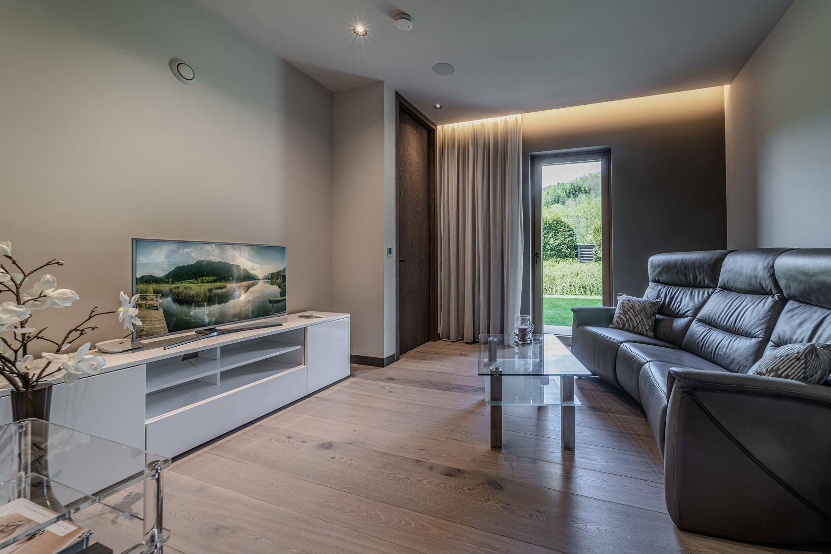 Gemütlicher Wohnbereich mit Sofa, Fernseher und Blick ins Grüne durch das Fenster.