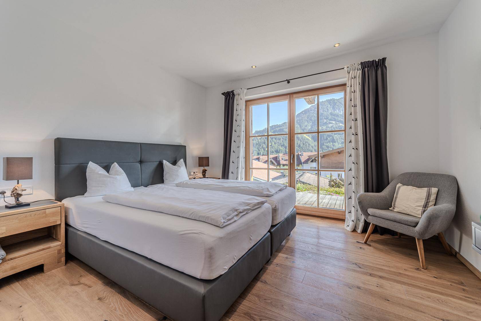 Schlafzimmer mit Holzboden, großen Fenstern und Bergblick.