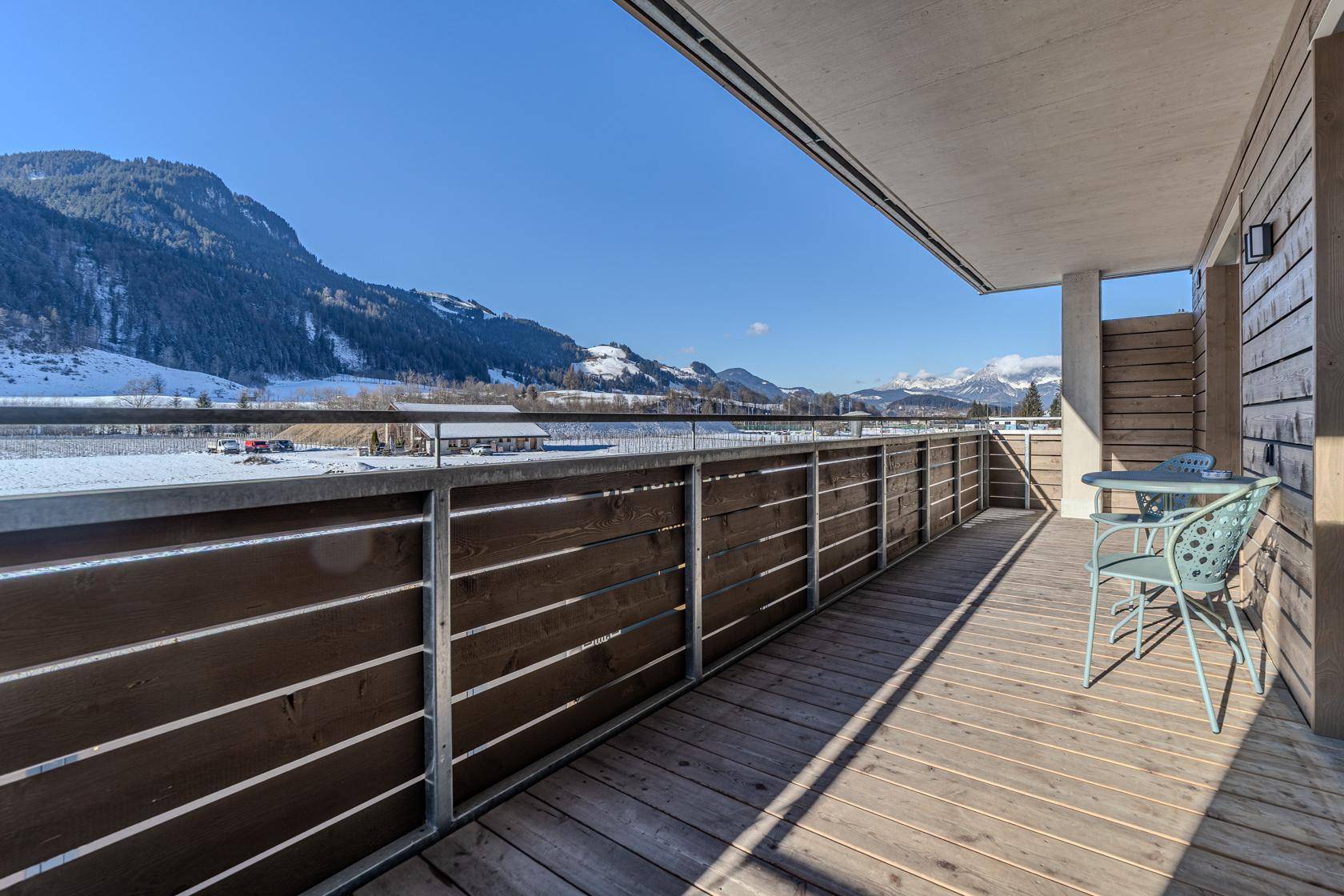 Großer Balkon mit Holzboden, Sitzgelegenheiten und Panoramablick auf die schneebedeckten Berge.