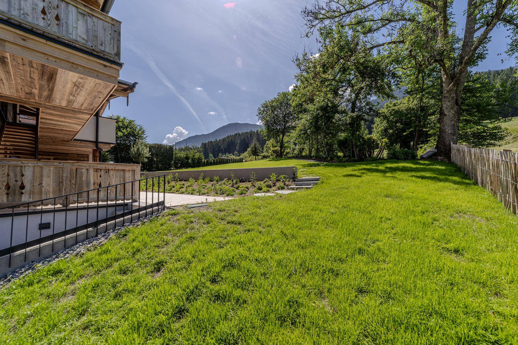 Gepflegter Gartenbereich mit Rasenfläche, Bepflanzung und Blick auf die umliegenden Berge.