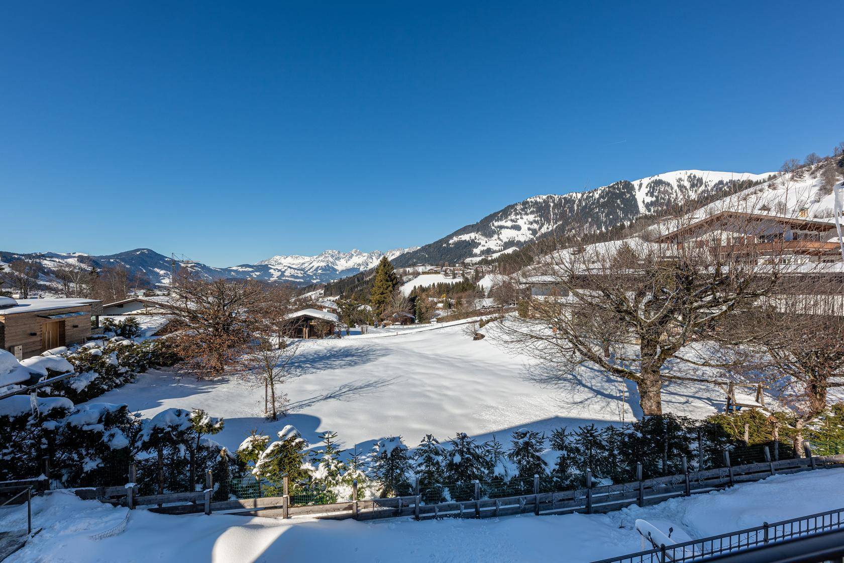 Weitläufiger Blick auf die verschneite Berglandschaft und umliegende Natur unter blauem Himmel.