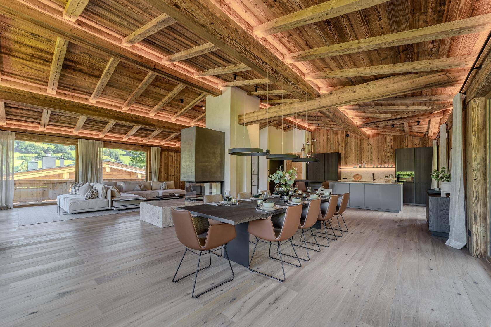 Offener Wohn-Essbereich mit Küche, Holzbalkendecke und Kamin in modernem Chalet-Stil.