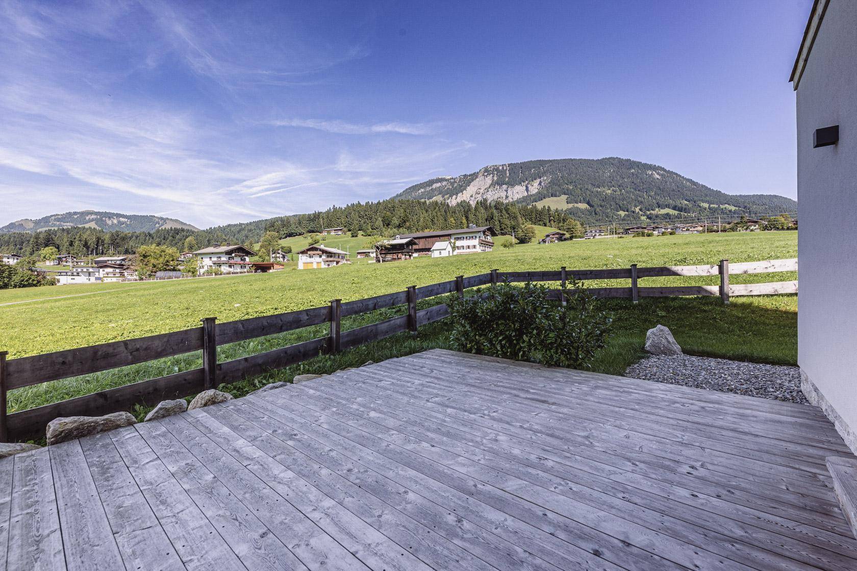 Holzterrasse mit Blick auf grüne Wiesen und die umliegende Berglandschaft.