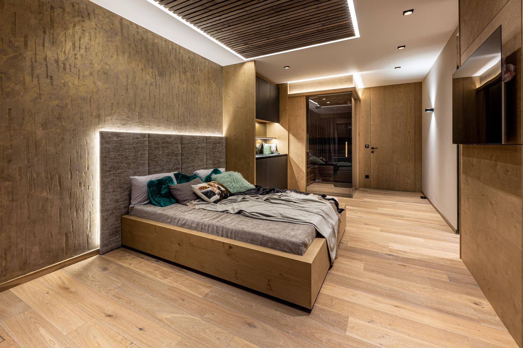 Stilvolles Schlafzimmer mit Holzboden, strukturierter Wand und indirekter Beleuchtung.