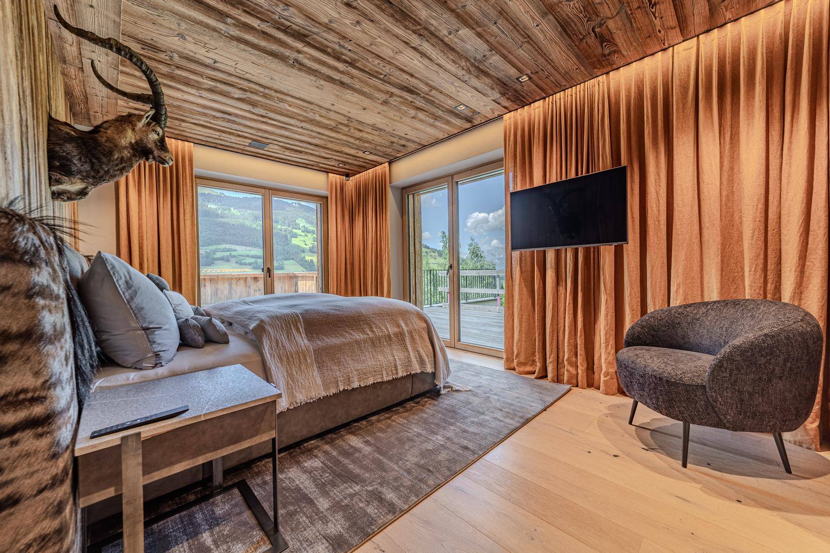 Helles Schlafzimmer mit Holzbalkendecke, großen Fenstern und Bergblick sowie traditioneller Dekoration.