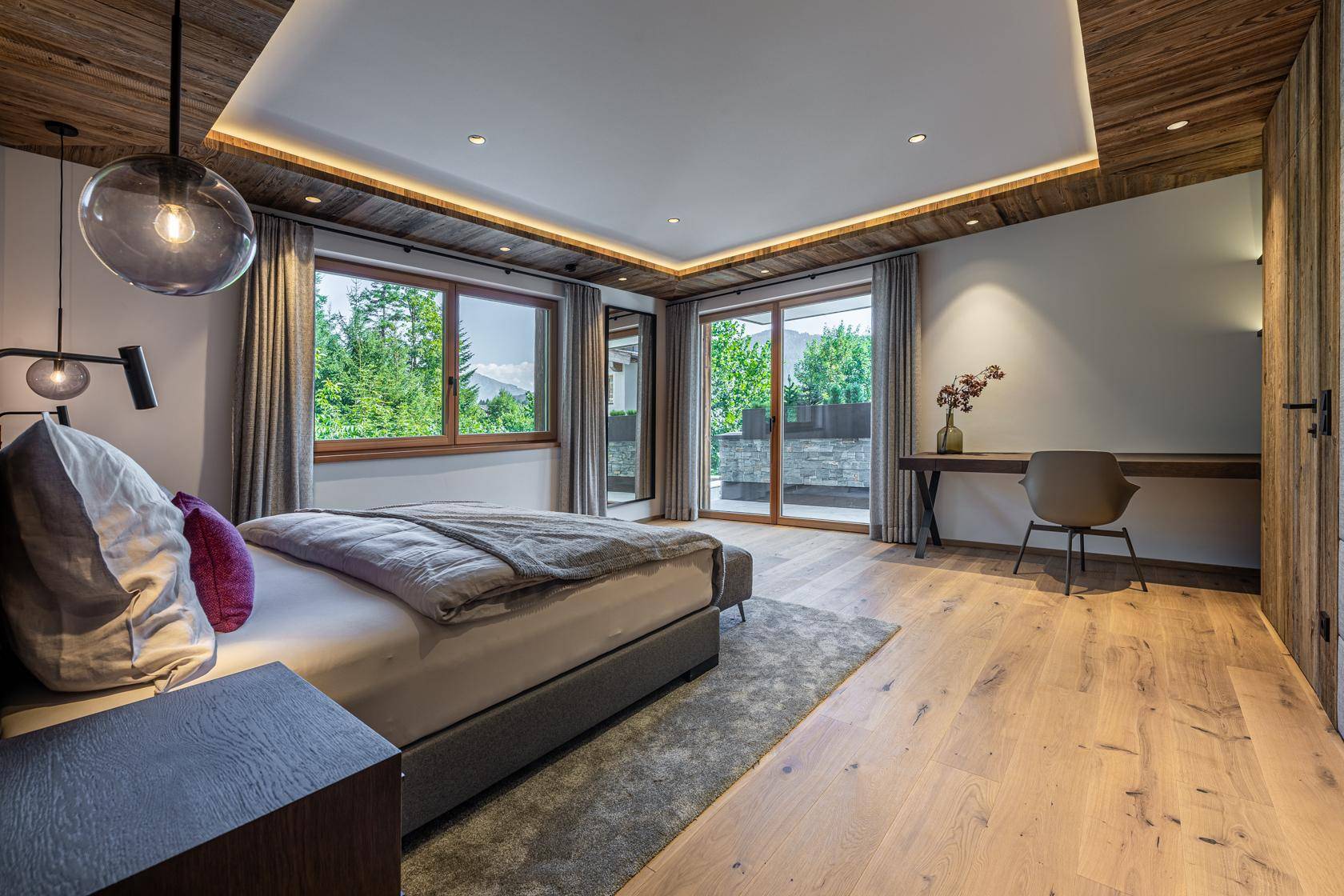 Helles Schlafzimmer mit Holzboden, Zugang zum Balkon und Blick ins Grüne.