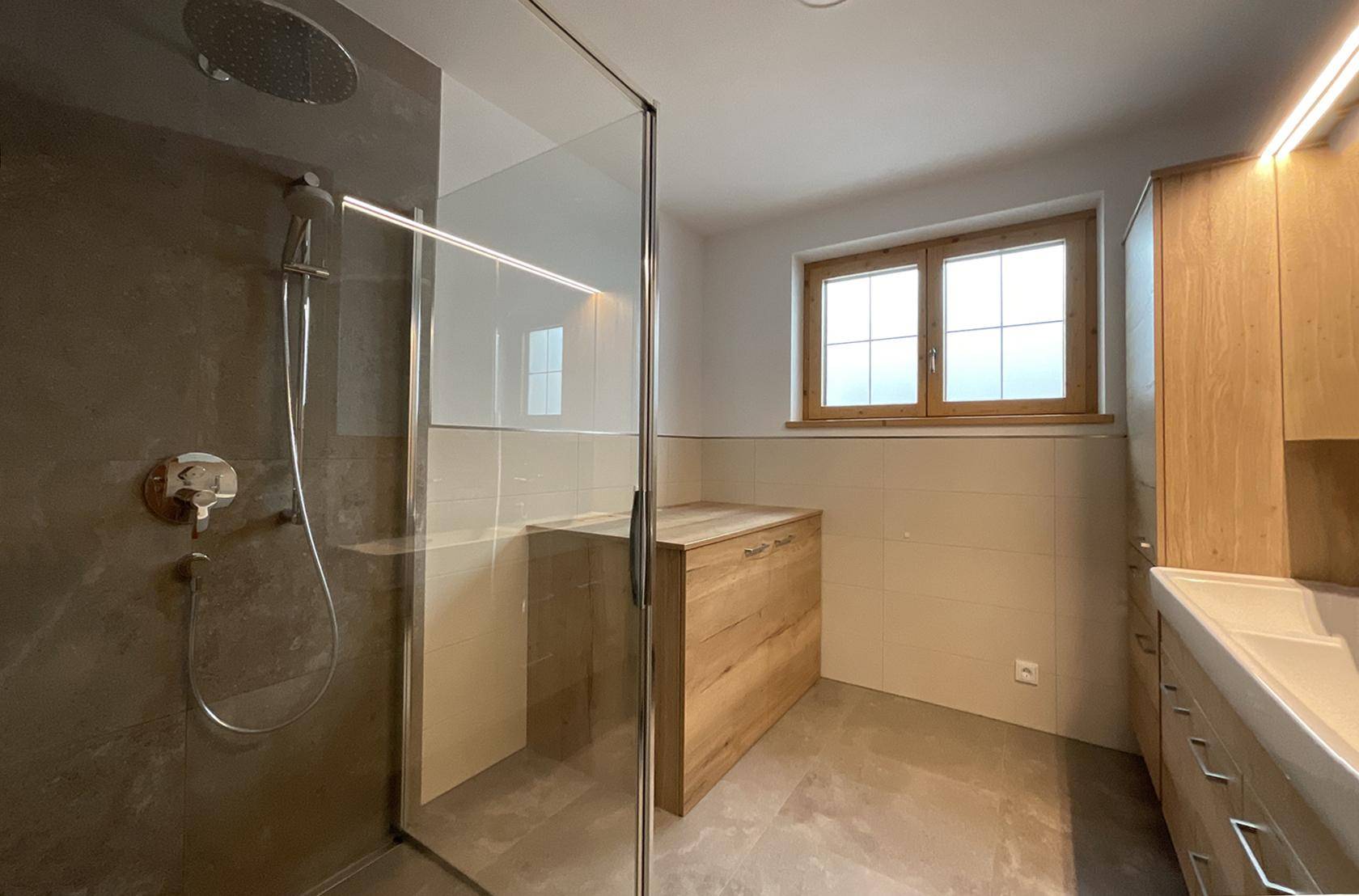 Modernes Badezimmer mit begehbarer Dusche, Fliesenboden und Holzwaschtischunterschrank, hell und funktional.