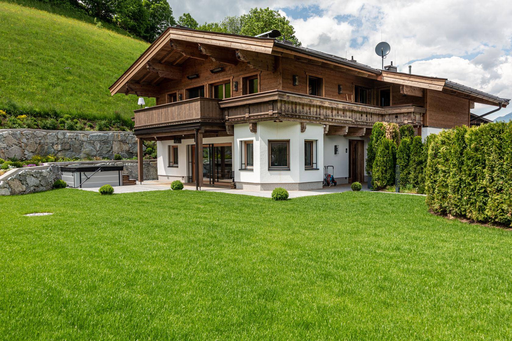 Großzügiger Gartenbereich mit Rasen, Whirlpool und traditioneller Holzfassade.