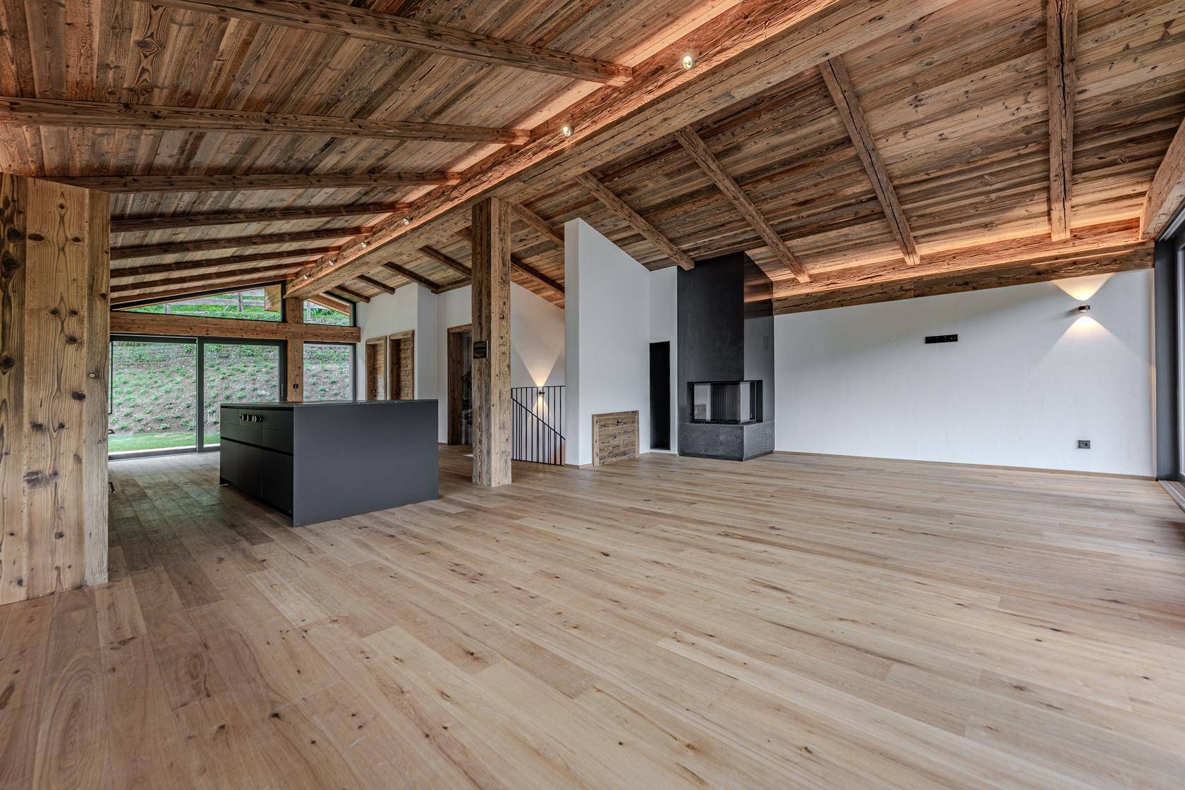 Offener Wohn-Essbereich mit moderner Küche, Kamin und Holzbalkendecke.