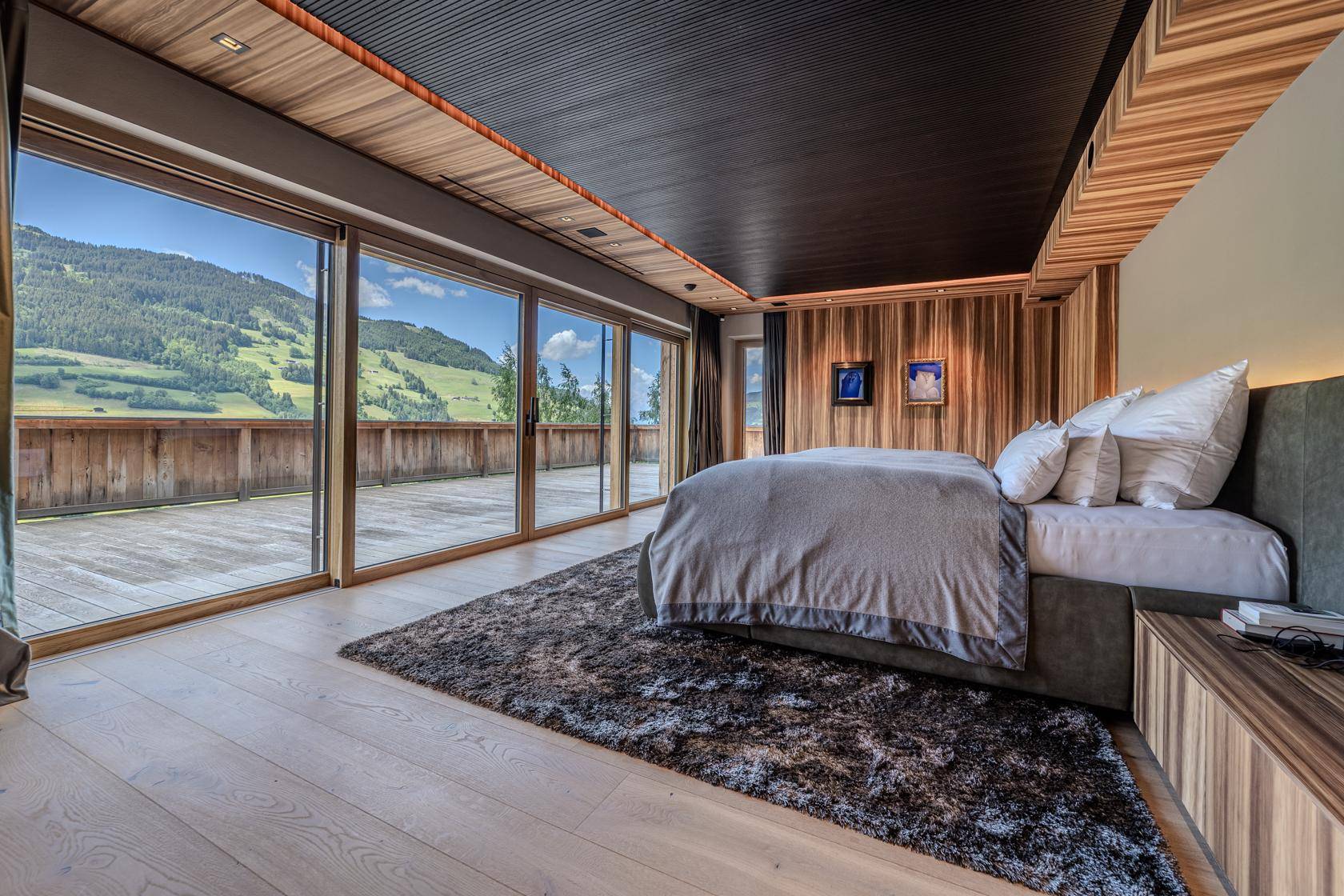 Geräumiges Schlafzimmer mit Holzwänden, großen Fenstern und direktem Zugang zur Terrasse mit Bergblick.
