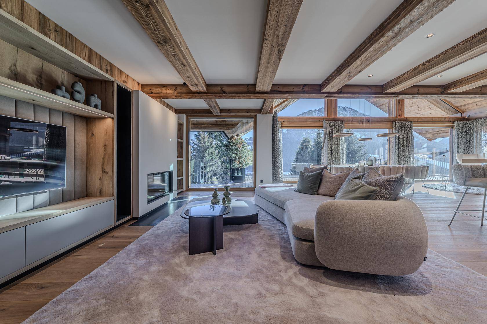 Gemütlicher Wohnbereich mit modernem Sofa, integriertem Kamin und Bergblick durch große Fenster.