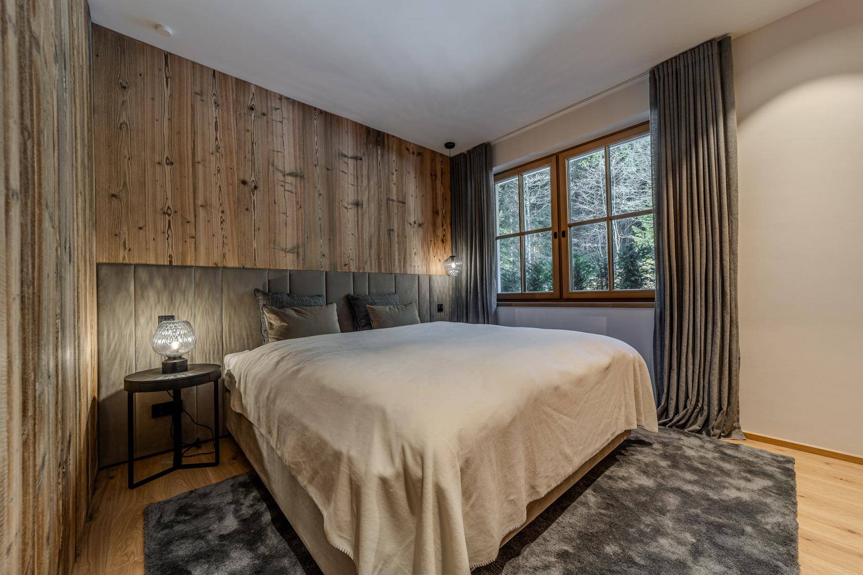 Ruhiges Schlafzimmer mit Holzwänden, großem Bett und Blick ins Grüne durch das Fenster.