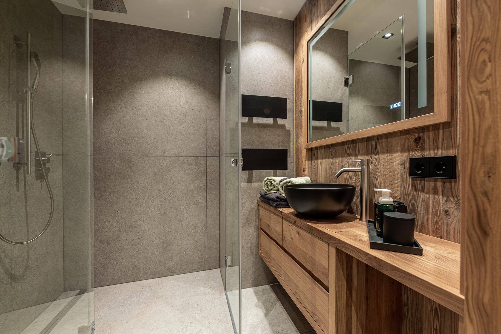 Modernes Badezimmer mit begehbarer Dusche, Holzwaschtisch und schwarzem Waschbecken.