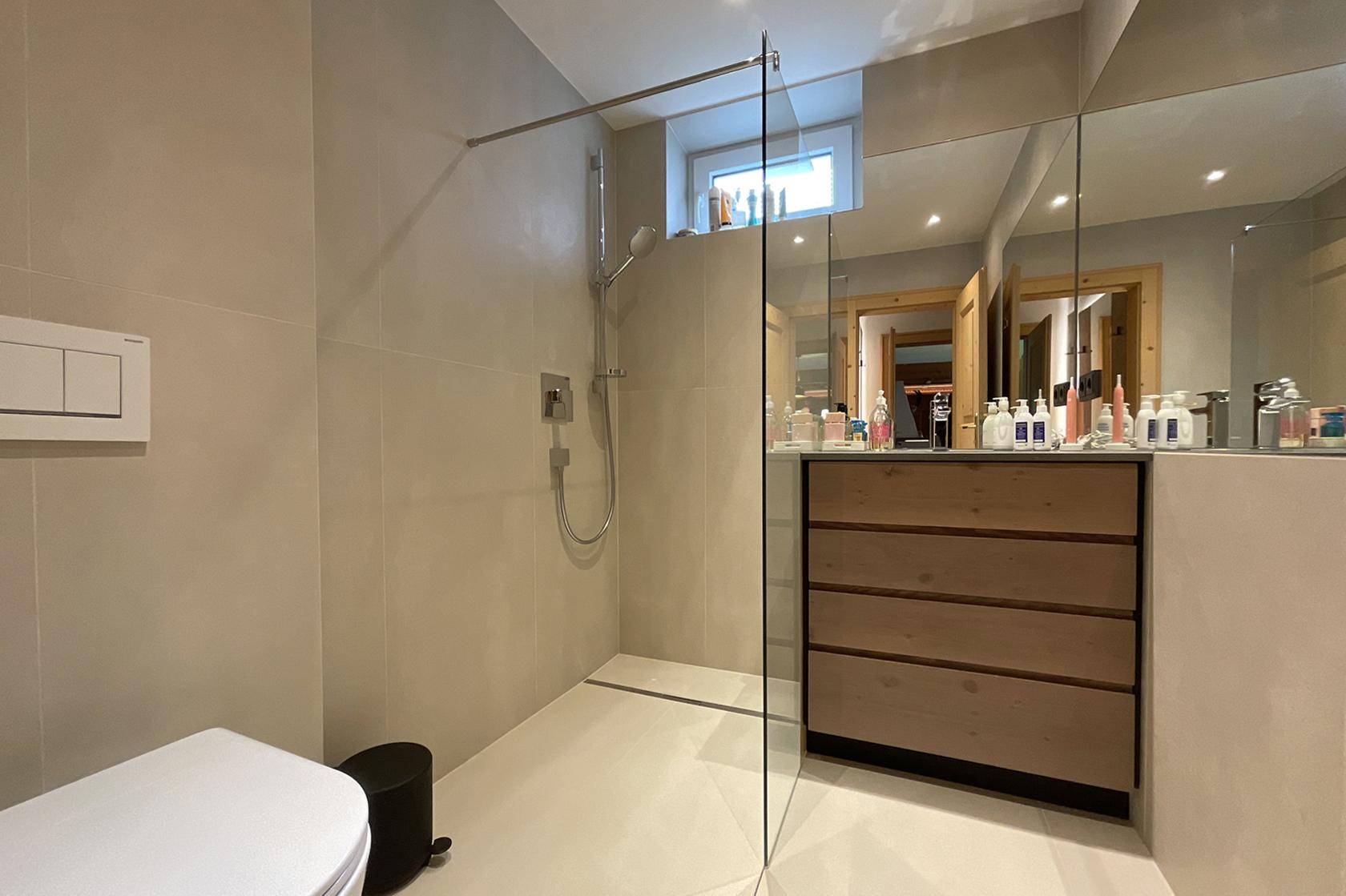 Modernes Badezimmer mit begehbarer Dusche, großem Spiegel und hellen Fliesen.