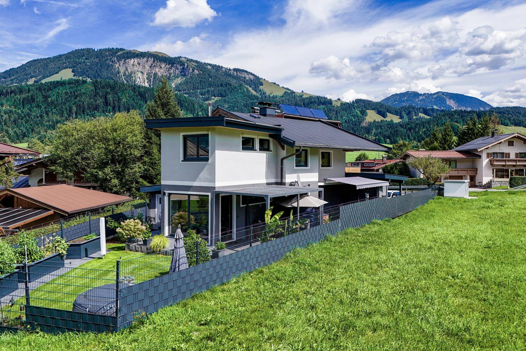 Modernes Einfamilienhaus mit Garten und Photovoltaikanlage, umgeben von grüner Natur.