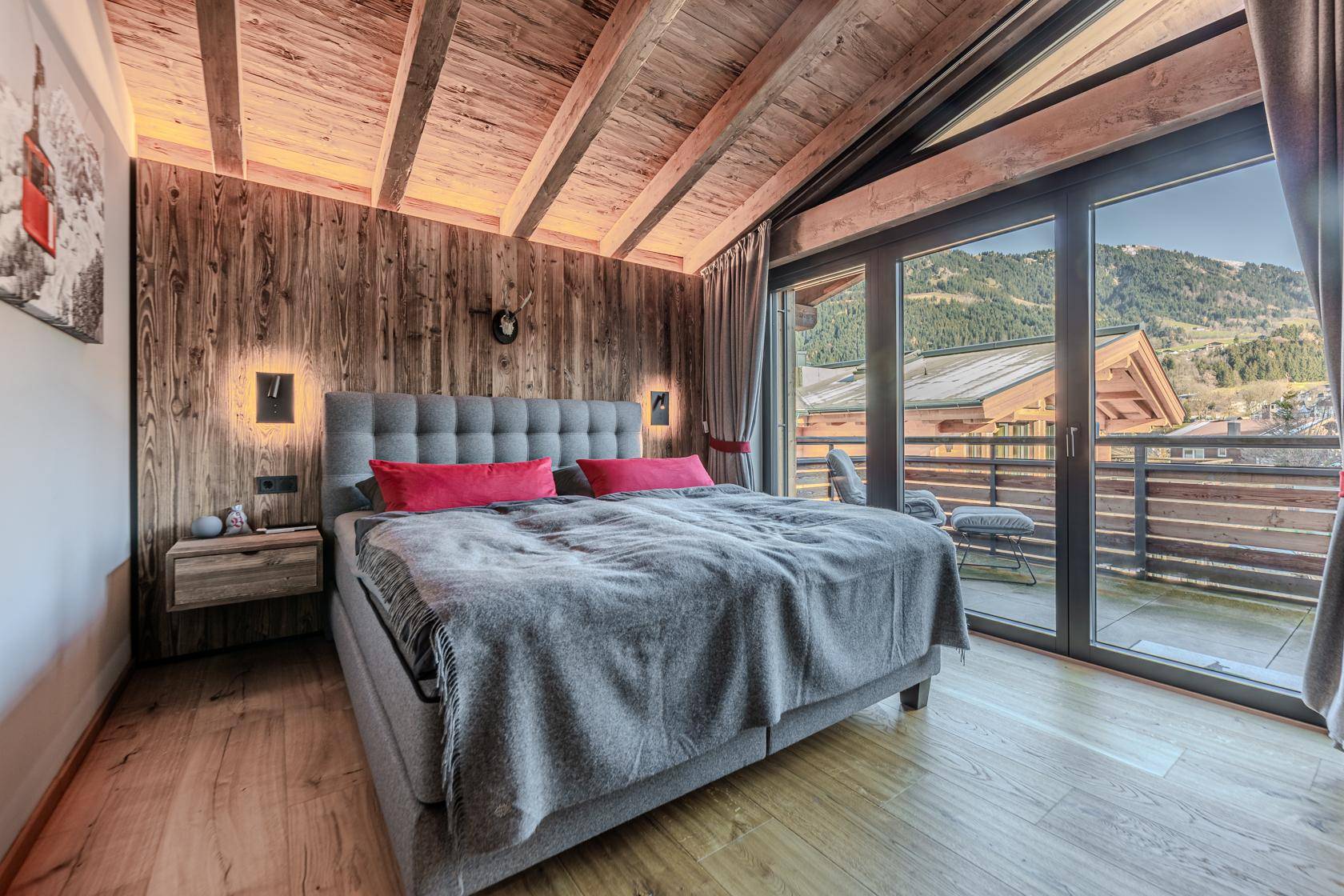 Helles Schlafzimmer mit Holzwand, großem Bett und Zugang zu einem Balkon mit Bergblick.