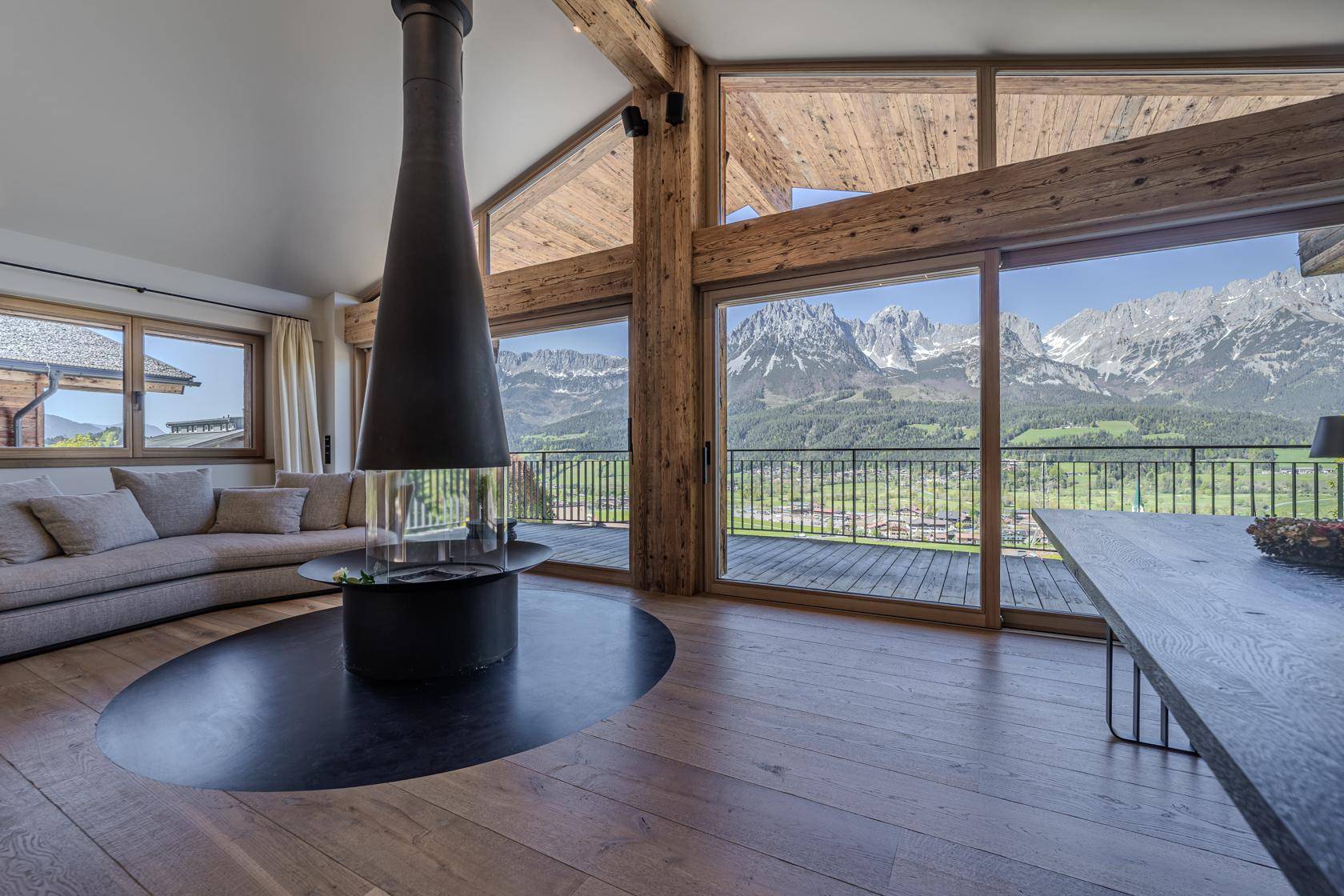 Helles Wohnzimmer mit Panoramablick auf die Berge, Holzboden und modernem Kamin.