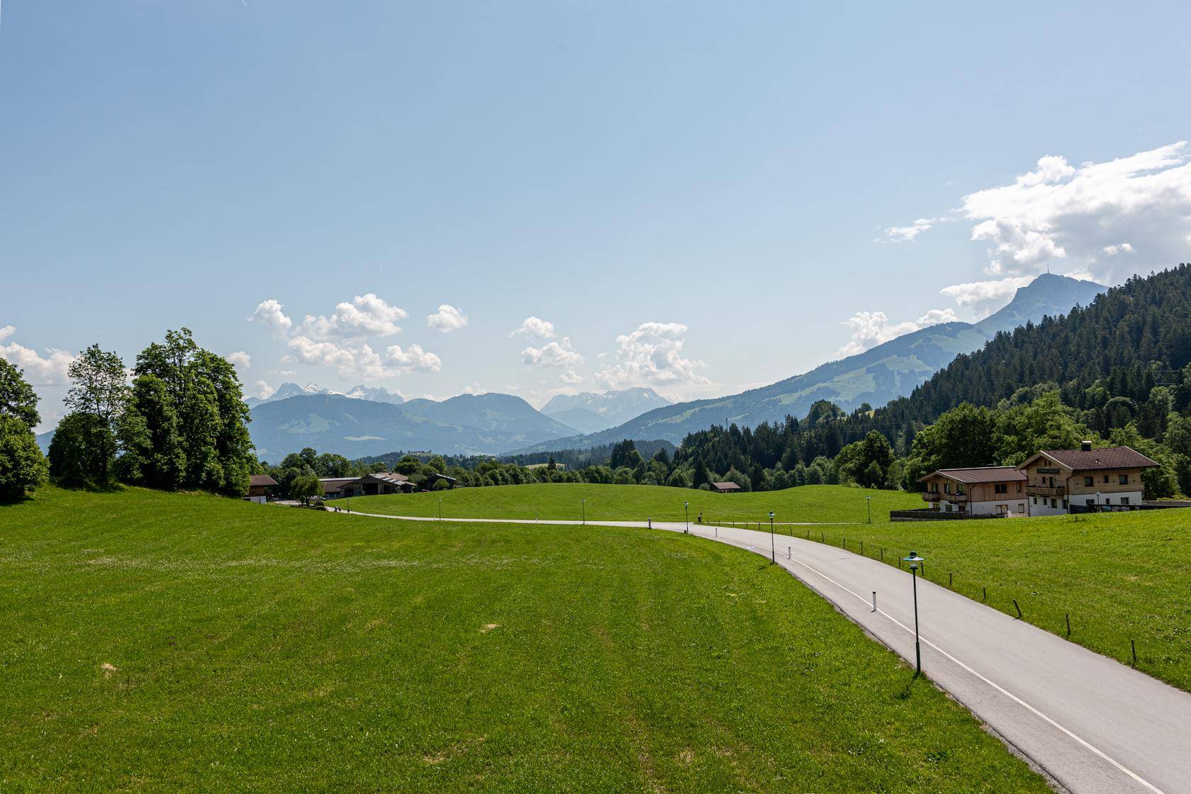 Malerische Landschaft mit grünen Wiesen, Bergen im Hintergrund und einer Landstraße.