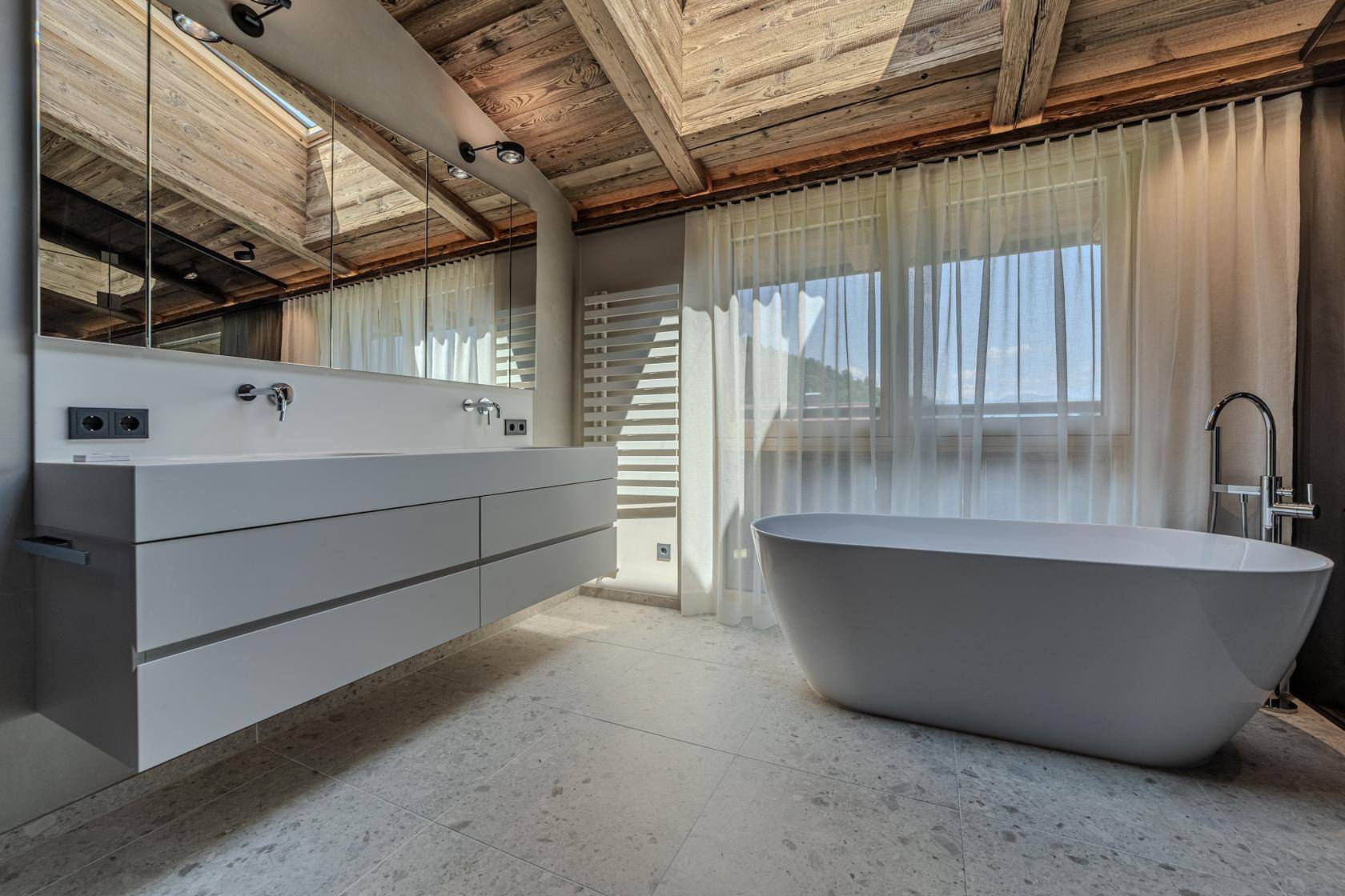 Modernes Badezimmer mit freistehender Badewanne, Doppelwaschbecken und Holzbalkendecke.