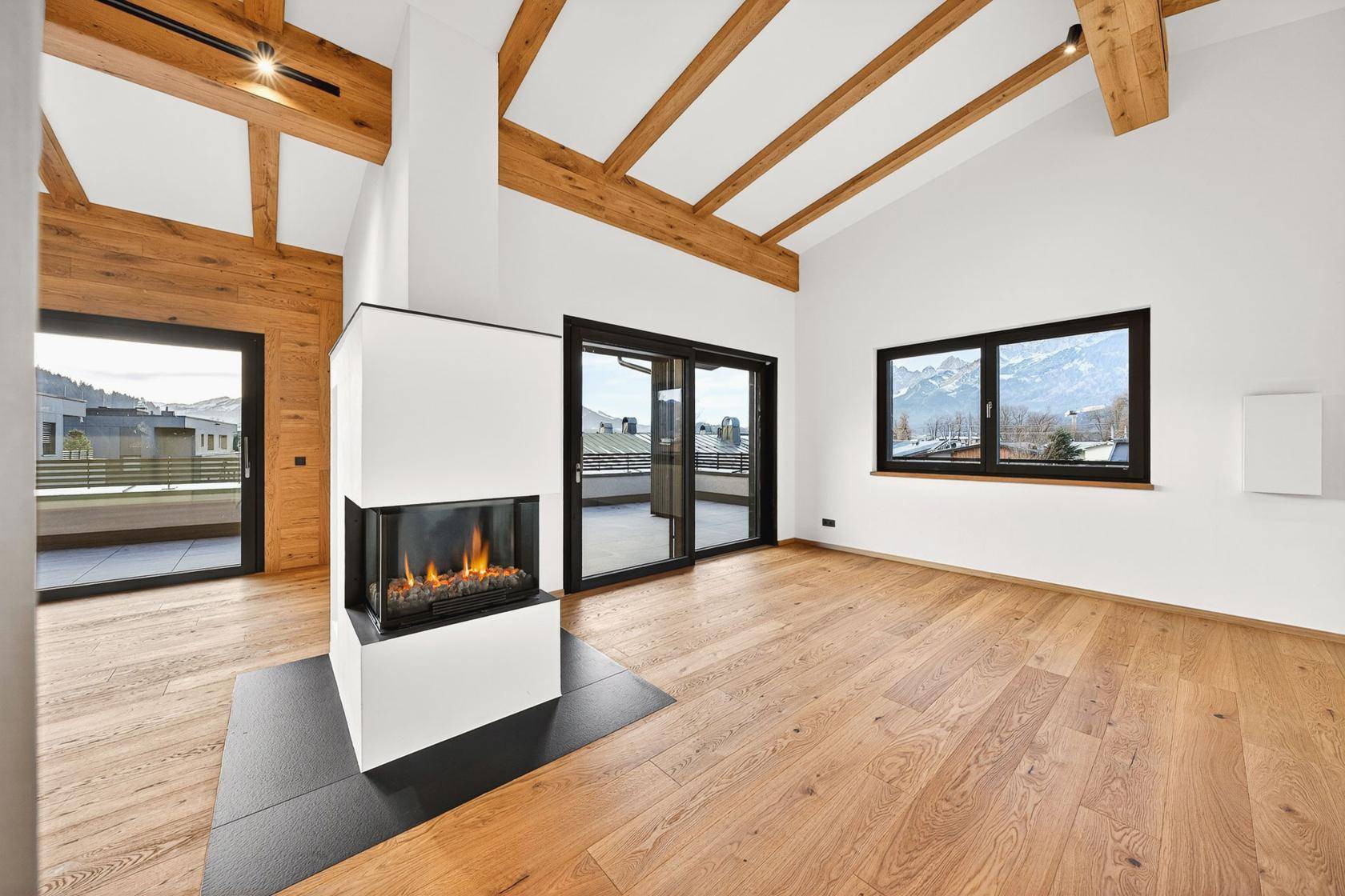 Offener Wohnbereich mit modernem Kamin, Holzbalkendecke und Zugang zur Terrasse mit Bergblick.