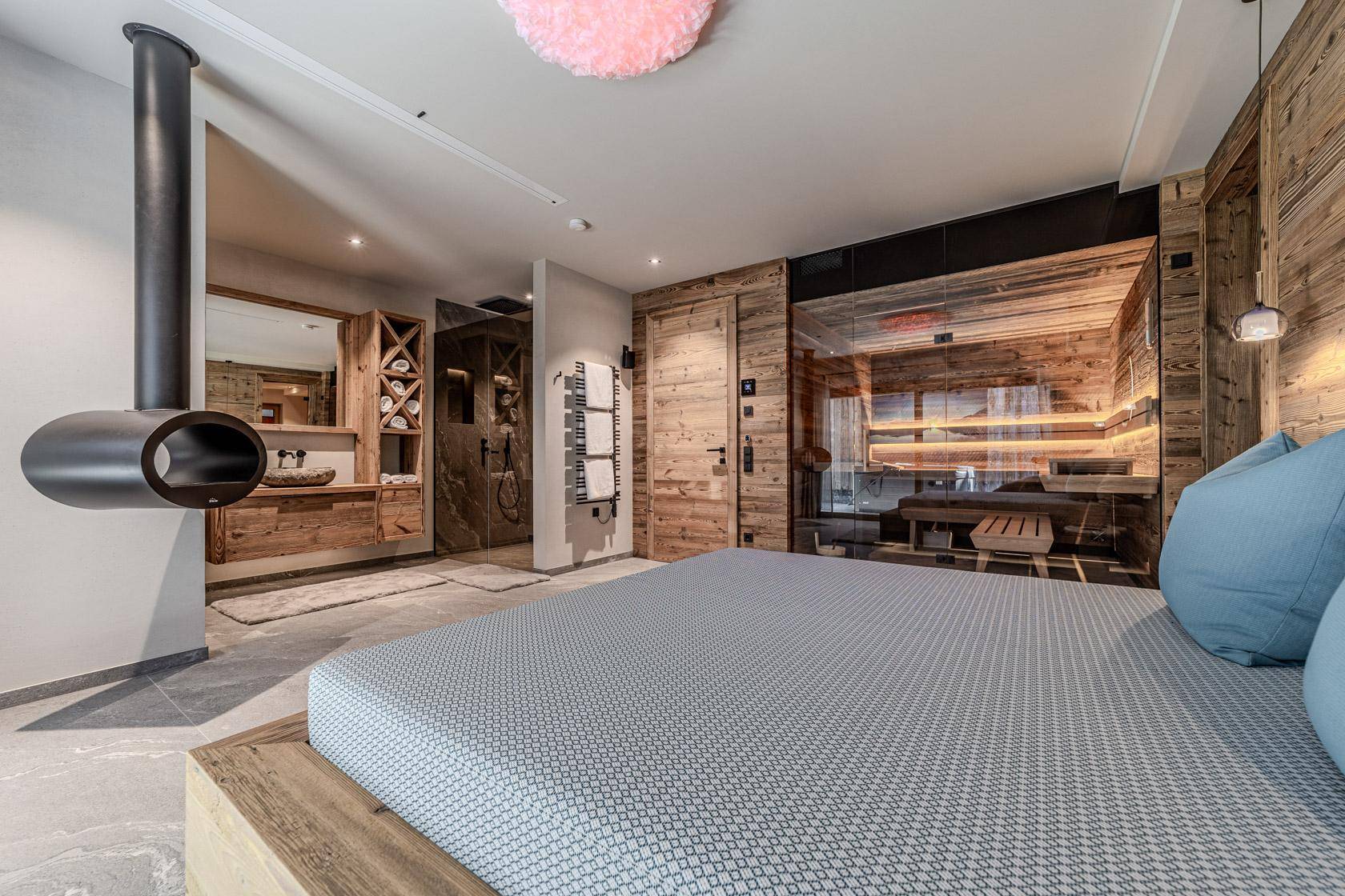 Schlafzimmer mit freihängendem Kamin, offenem Badbereich und direkter Sauna-Zugang.
