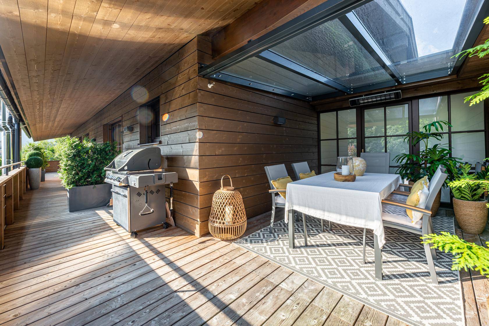 Geräumige Holzterrasse mit Grillbereich, Esstisch und Überdachung für entspannte Stunden.