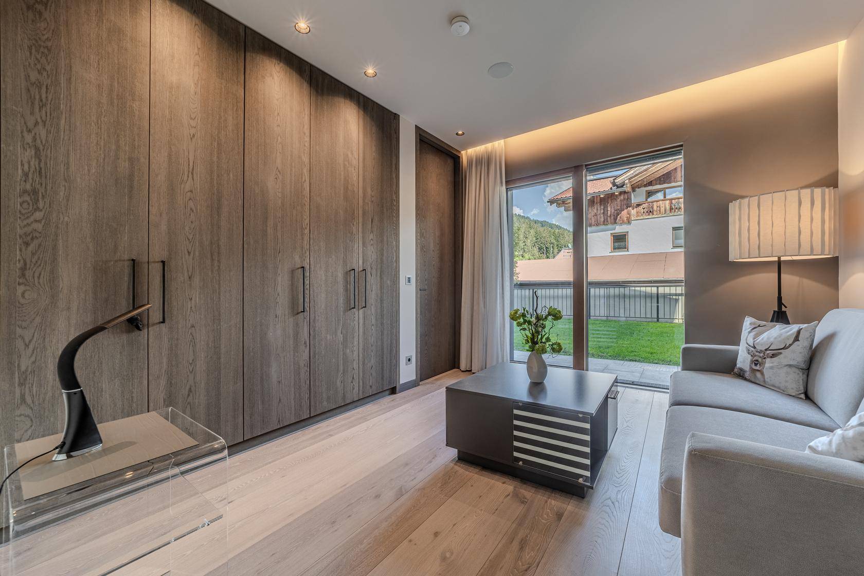 Helles Schlafzimmer mit Einbauschränken, Sofa und Zugang zu einem kleinen Balkon.