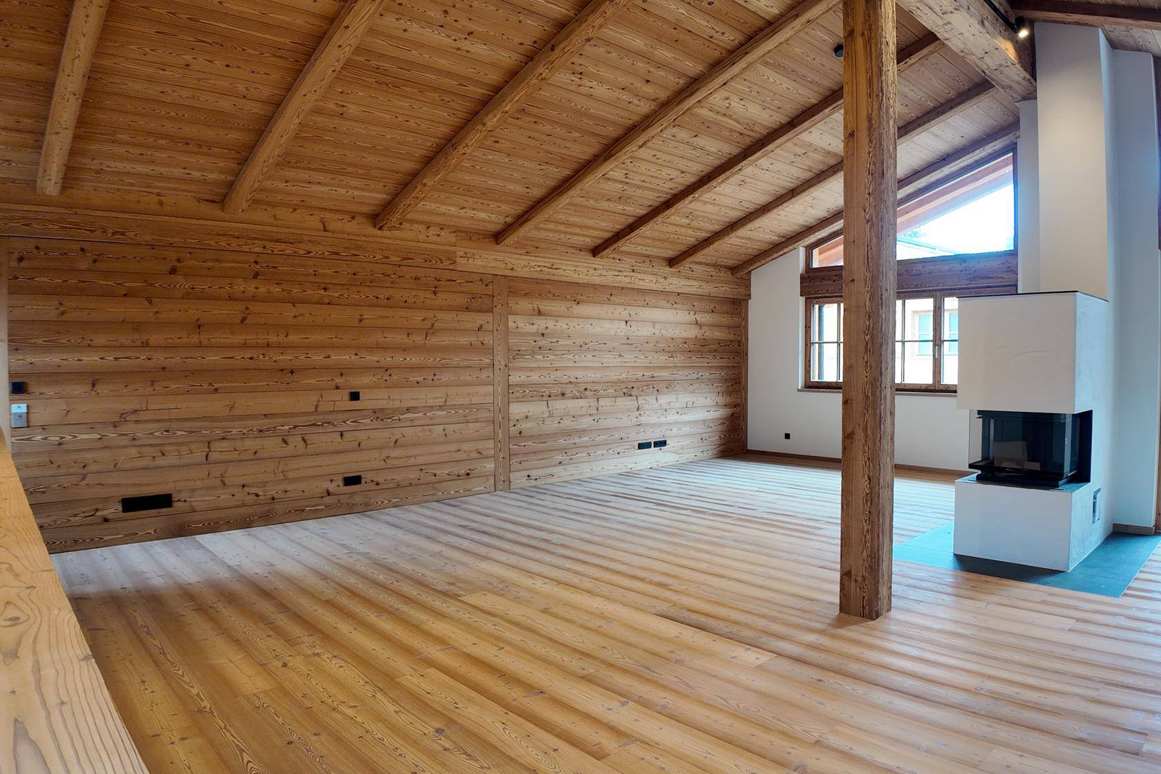 Heller Wohnraum mit Holzwänden, Holzboden und einem modernen Kamin, der eine gemütliche Atmosphäre schafft.