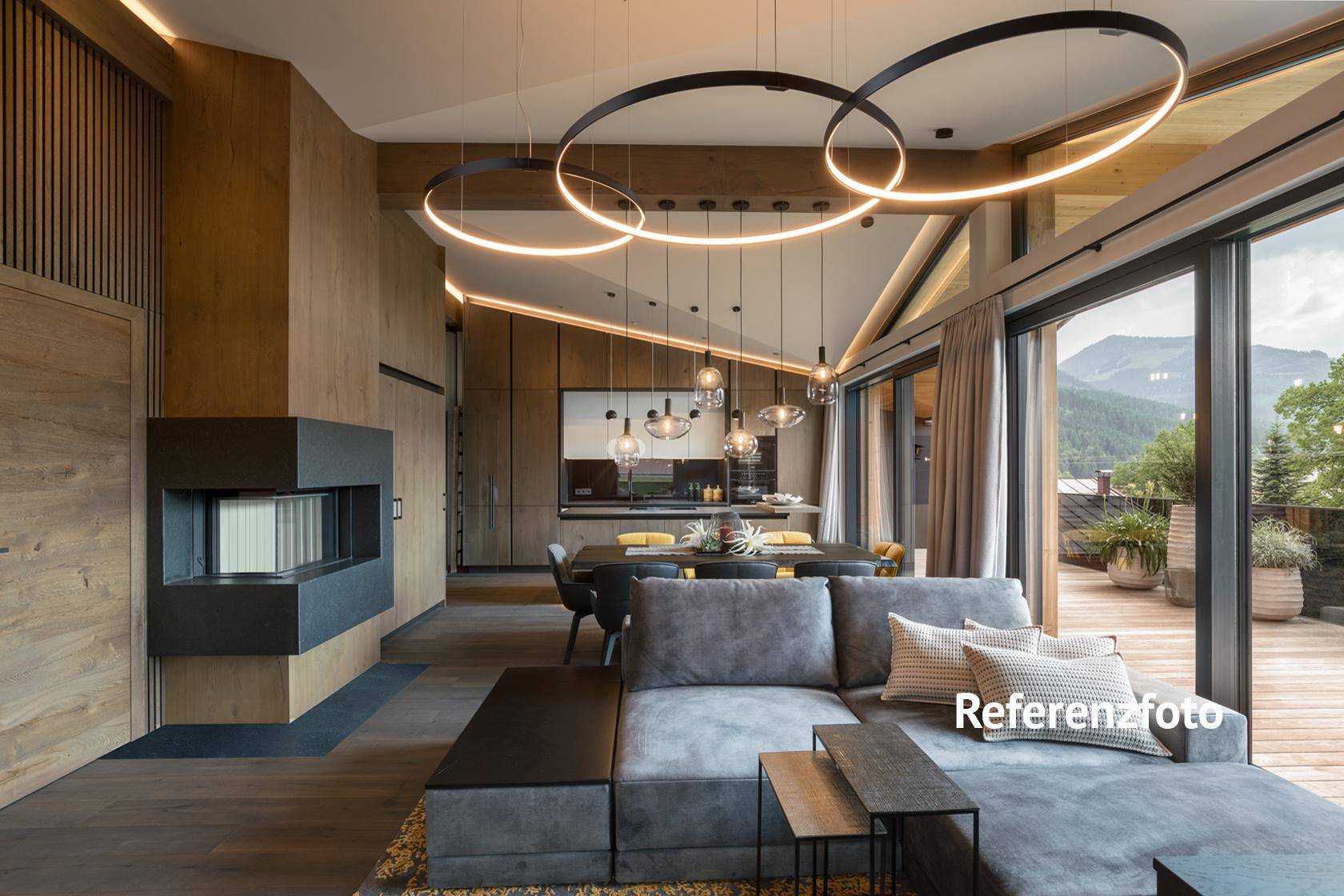 Großzügiger Wohn-Essbereich mit Kamin, Holzelementen und Zugang zu einer Terrasse mit Bergblick.