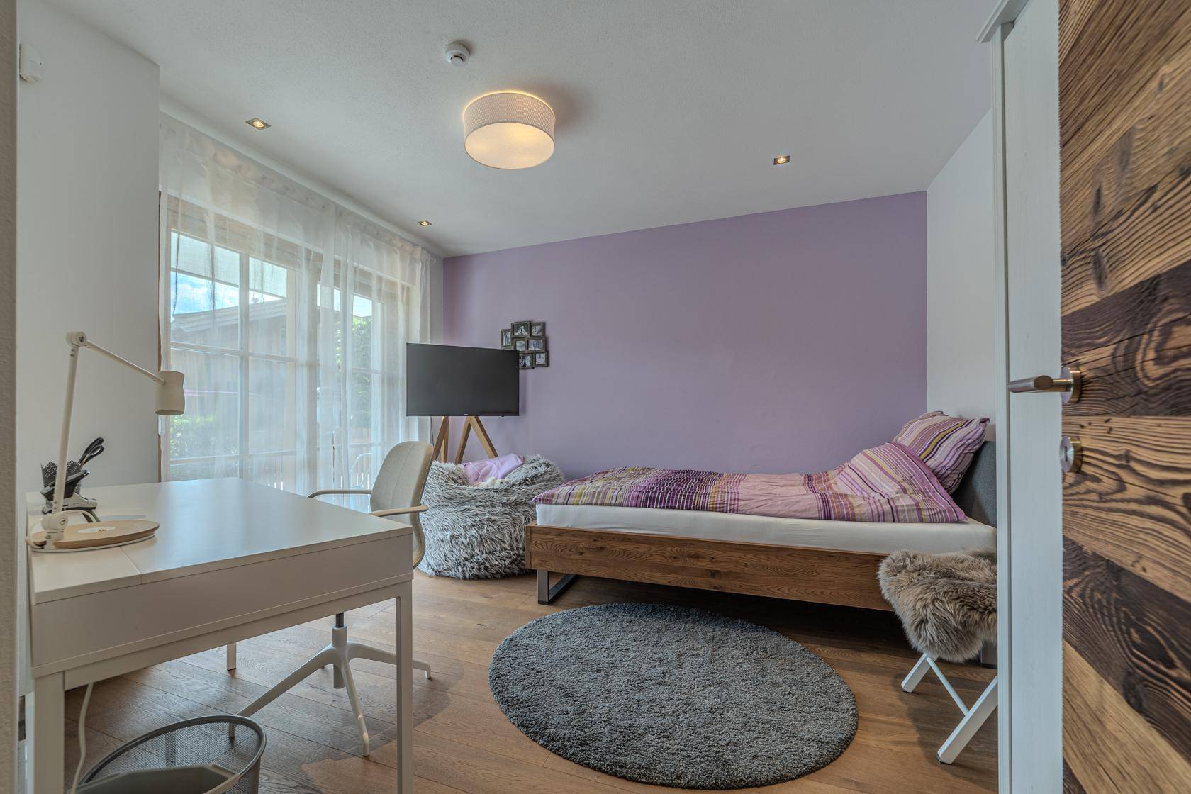 Helles Schlafzimmer mit Holzbett, Schreibtisch und Zugang zu einem Balkon.