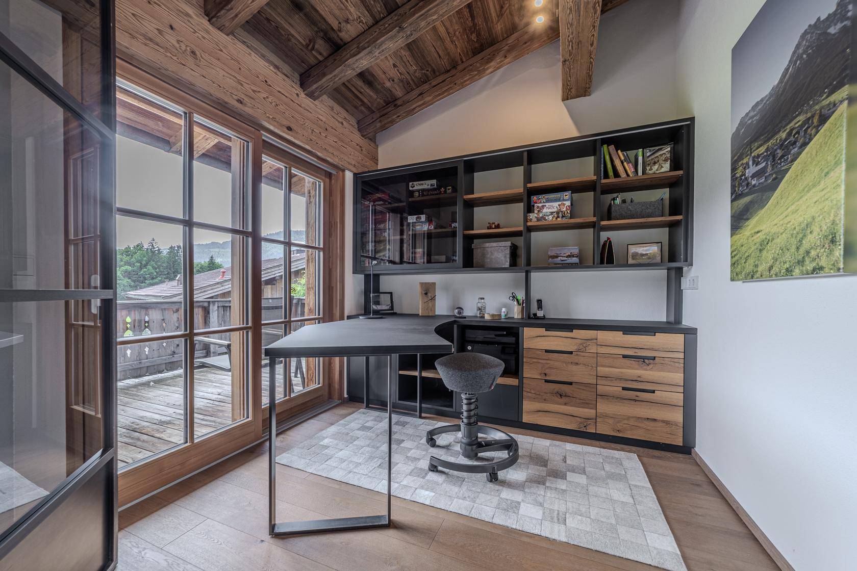 Modernes Arbeitszimmer mit Holzbalkendecke, großem Fenster und Zugang zu einem Balkon.