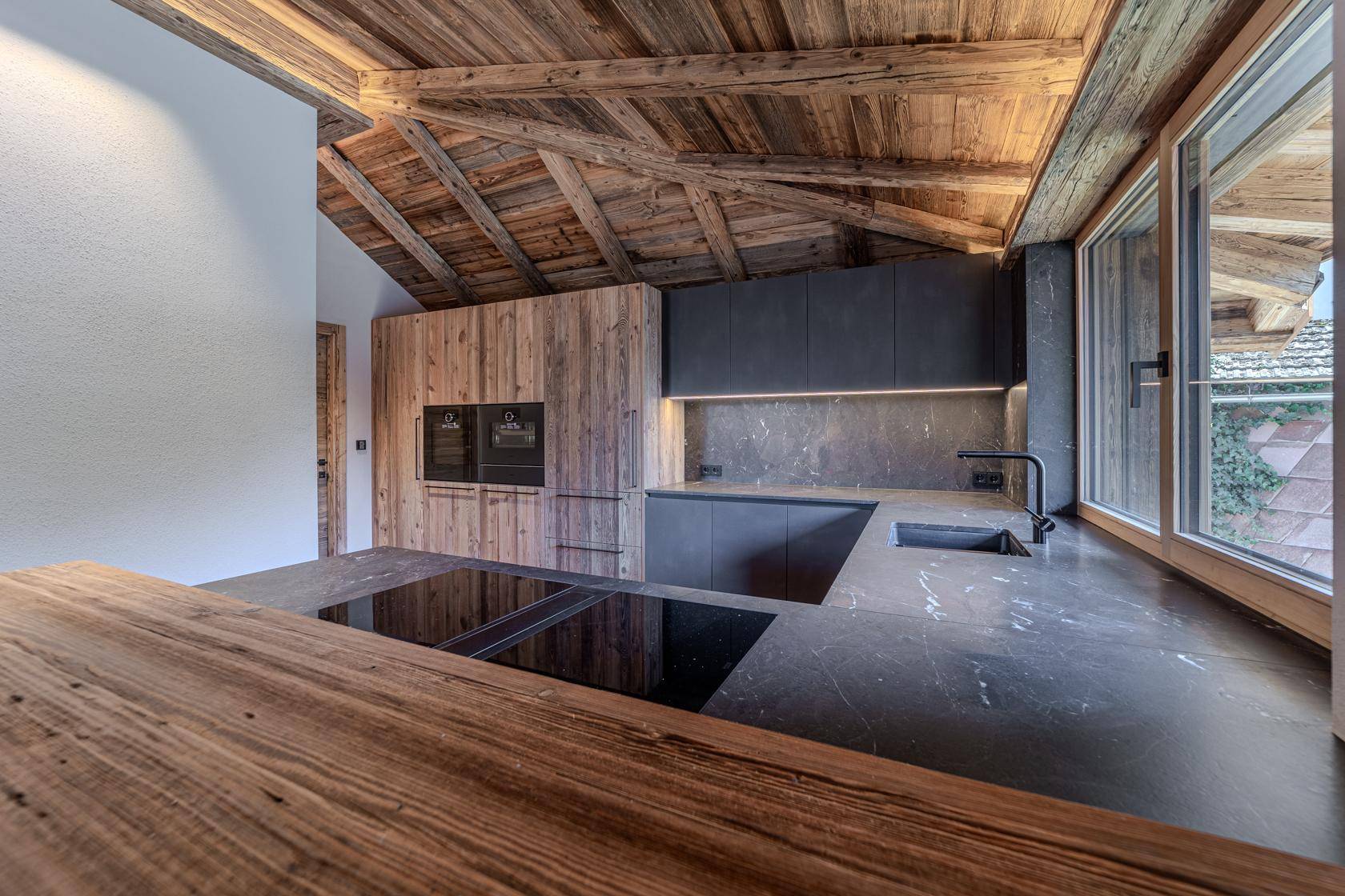Kücheninsel mit Induktionskochfeld und Holz-Frühstücksbar, umgeben von modernen dunklen Arbeitsplatten und Schränken.