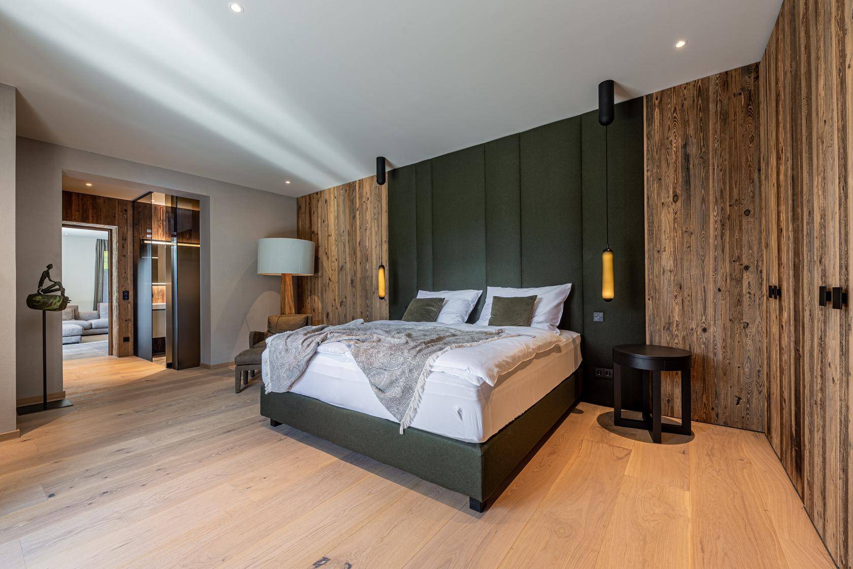 Elegantes Schlafzimmer mit Holzwänden, grünem Kopfteil und hellem Holzboden, mit Zugang zum Wohnbereich.