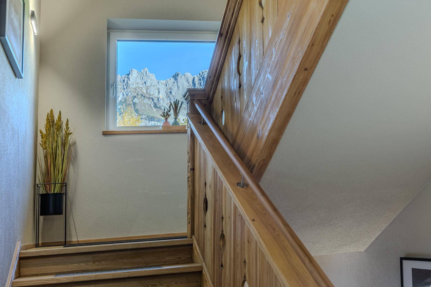 Rustikale Holztreppe mit geschnitztem Geländer und Fensterblick auf die umliegenden Berge.