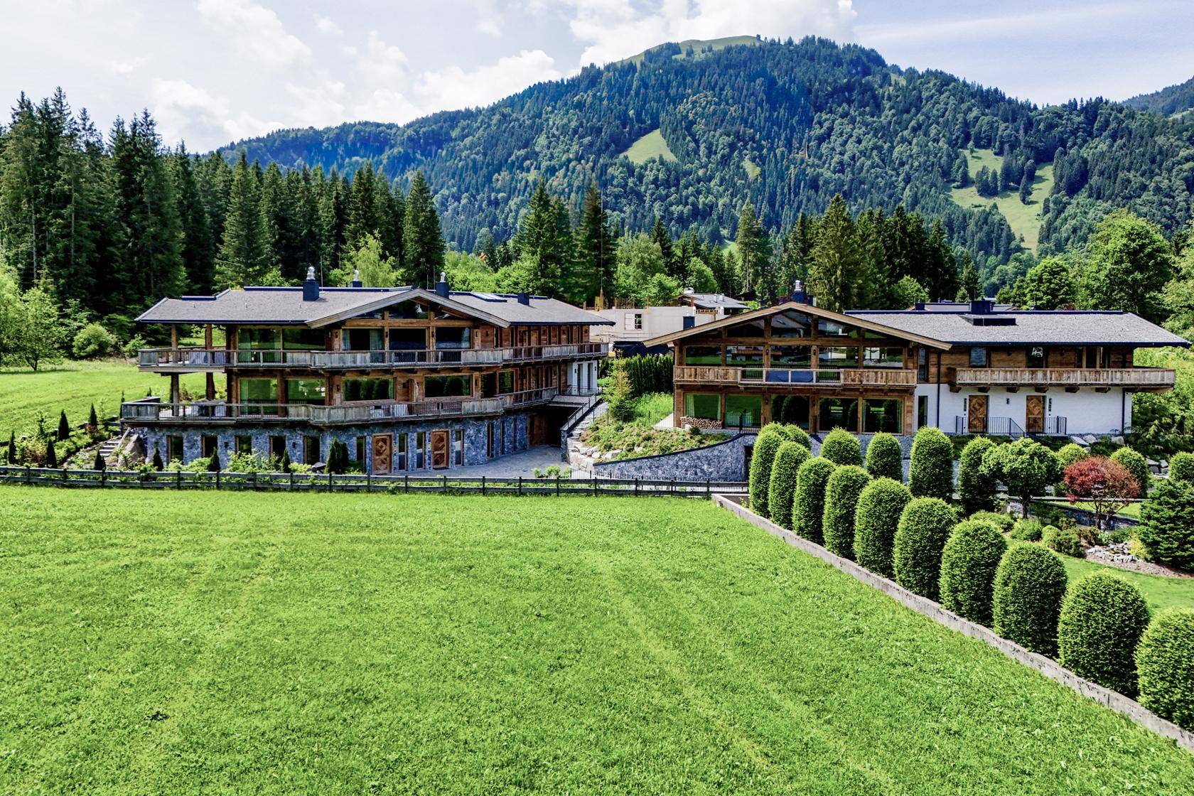Zwei luxuriöse Chalets in weitläufiger alpiner Umgebung mit grünen Wiesen und Bergblick.