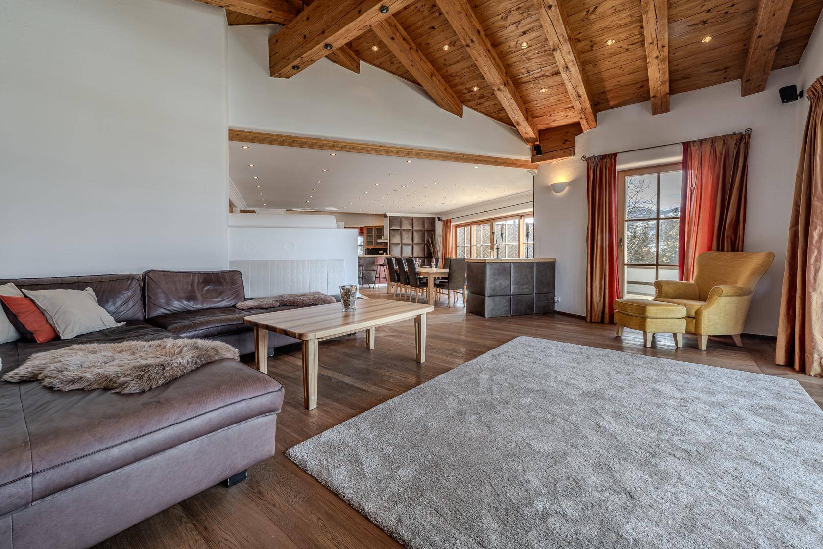 Offener Wohnbereich mit Ledersofa, Holzboden und Blick auf den Essbereich im Hintergrund.