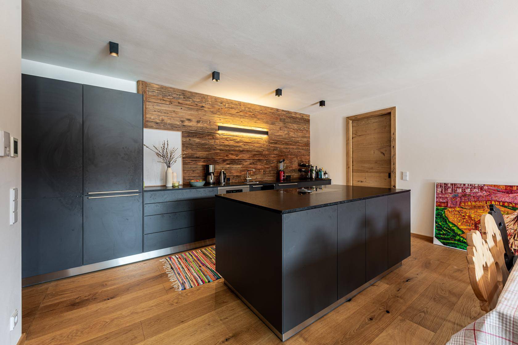 Moderne Küche mit dunklen Fronten, Holzrückwand und großer Kücheninsel.