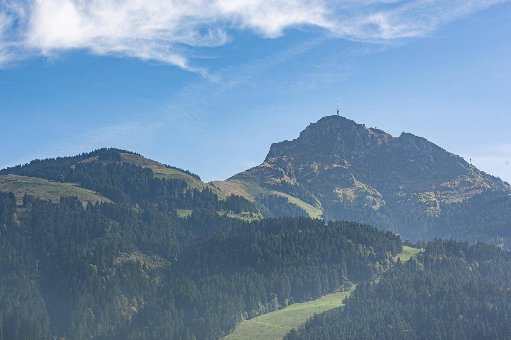 Malerischer Blick auf die umliegende Berglandschaft mit grünen Wäldern und blauem Himmel.