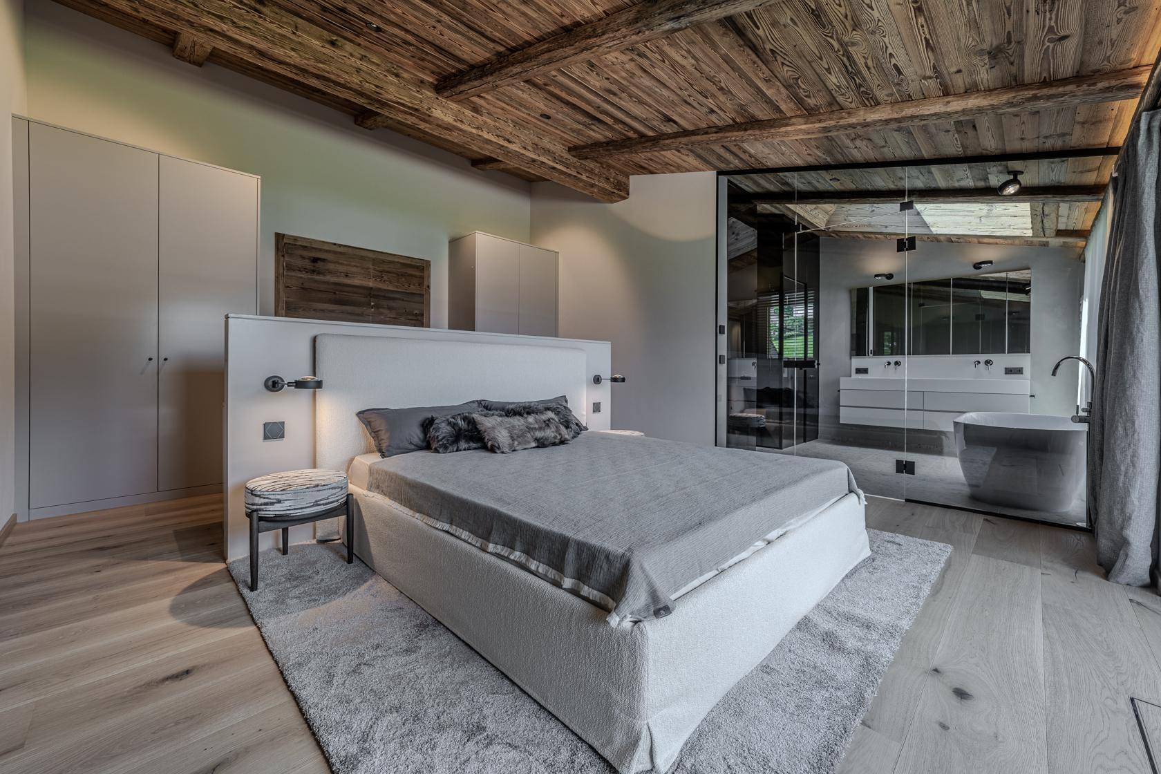 Elegantes Schlafzimmer mit Holzbalkendecke und integriertem Badezimmer hinter Glaswand.