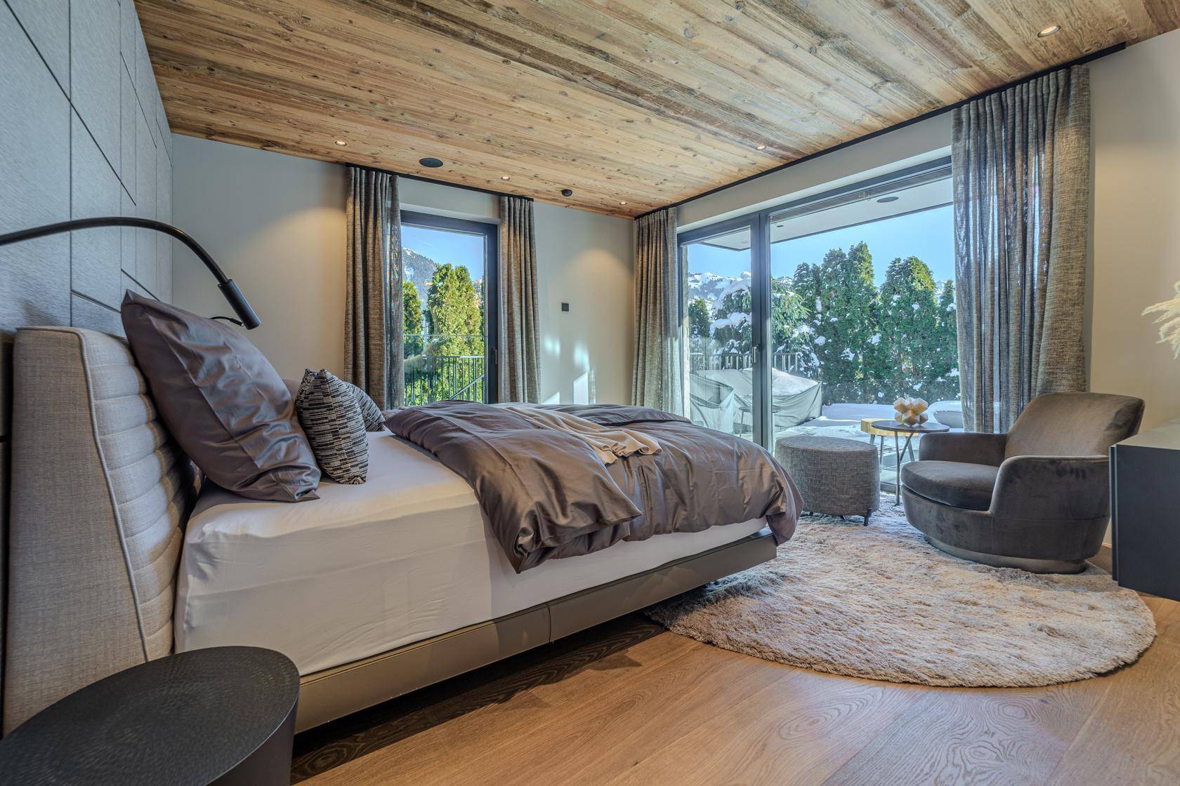 Gemütliches Schlafzimmer mit Holzbalkendecke, großem Bett und Zugang zu einem Balkon mit Bergblick.