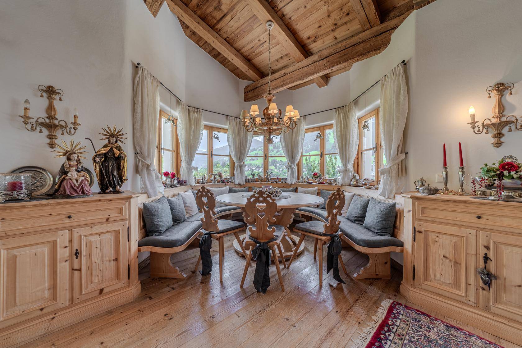 Heller Essbereich mit runder Sitzecke, Holztisch und Fenstern mit Blick auf die grüne Landschaft.