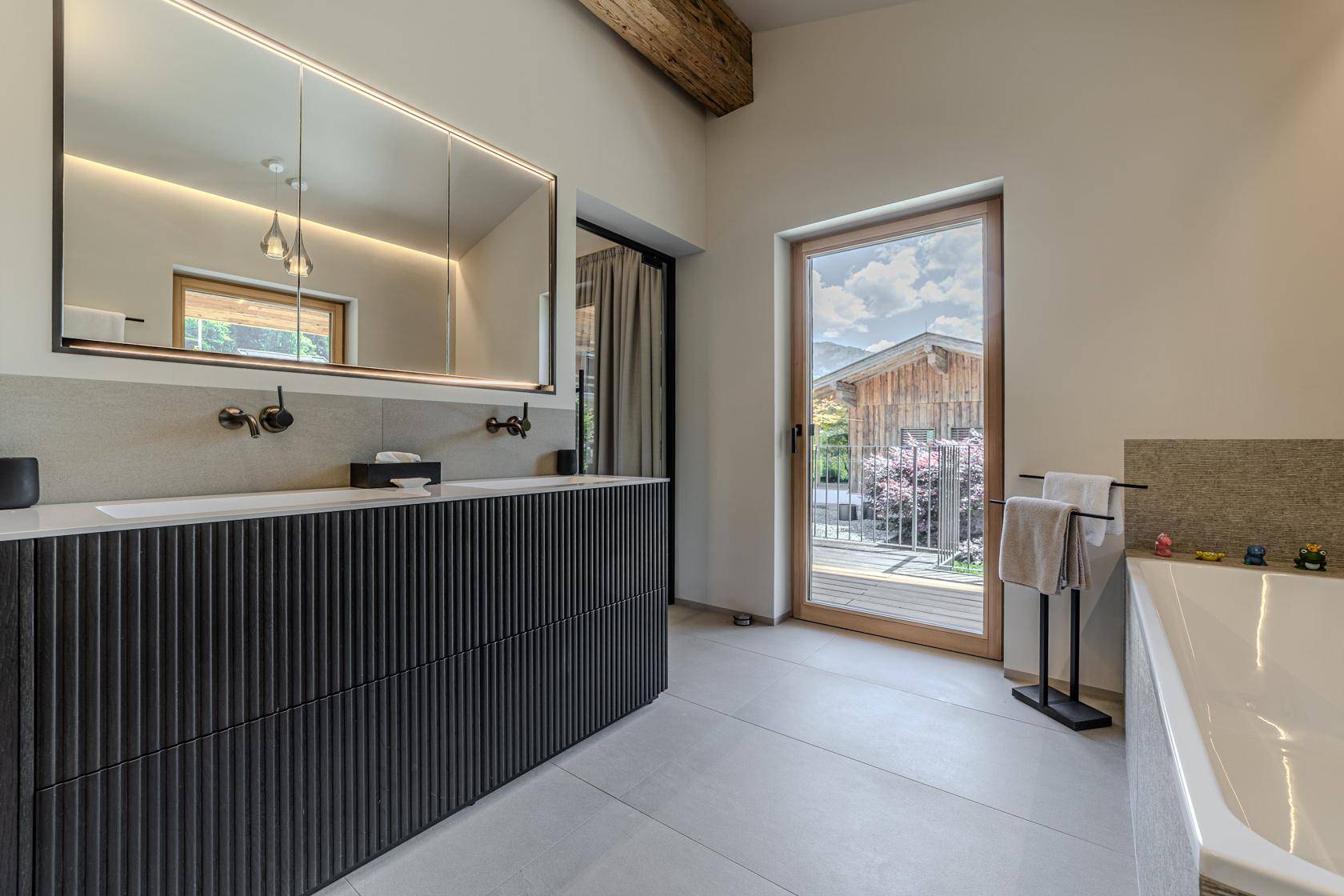Elegantes Badezimmer mit modernem Waschtisch, großem Spiegel und Zugang zu einem Außenbereich.